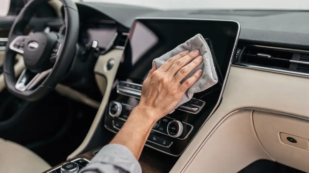 Auto-Display reinigen: Mikrofasertuch an einem Touchscreen im Auto-Innenraum
