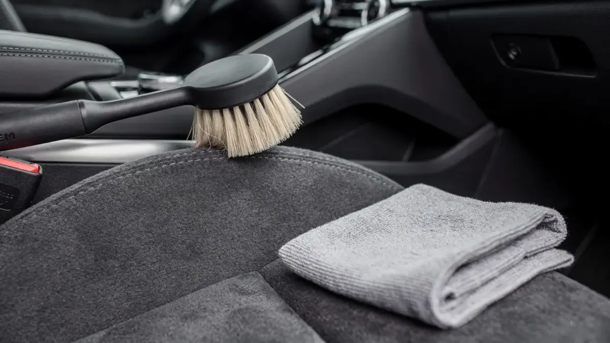 Alcantara im Auto reinigen: Detail einer gepflegten Fahrzeugoberfläche mit Bürste und Mikrofasertuch