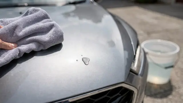 Vogelkot am Auto wird mit einem Mikrofasertuch vom Lack entfernt.